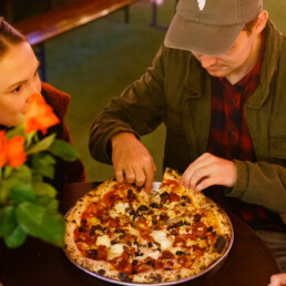 Two customerCouple eating a pizza in the Franciscan Well beer garden where table booking is not required