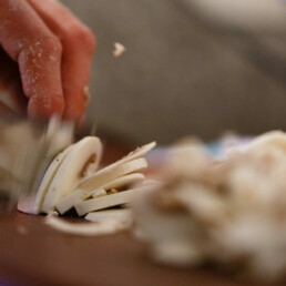 Close-up of staff members hands slicing mushroom pizza toppings