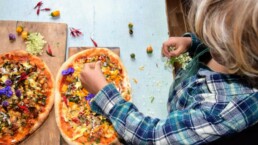 child putting finishing touches on pizza made at home with pompeii pizza kit